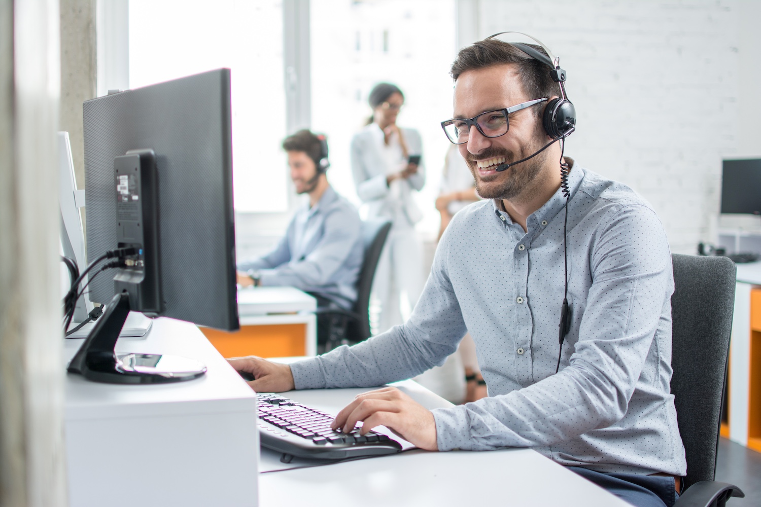 Smiling customer support operator with hands-free headset working in the office.