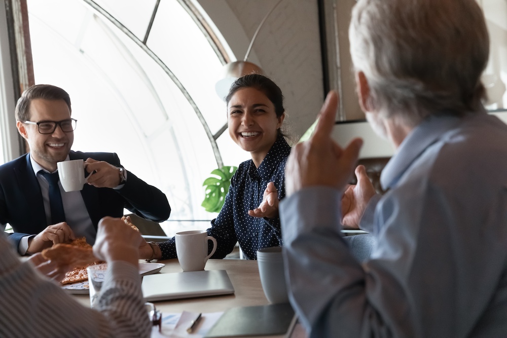 Happy friendly multi-ethnic staff group enjoy eating pizza in office