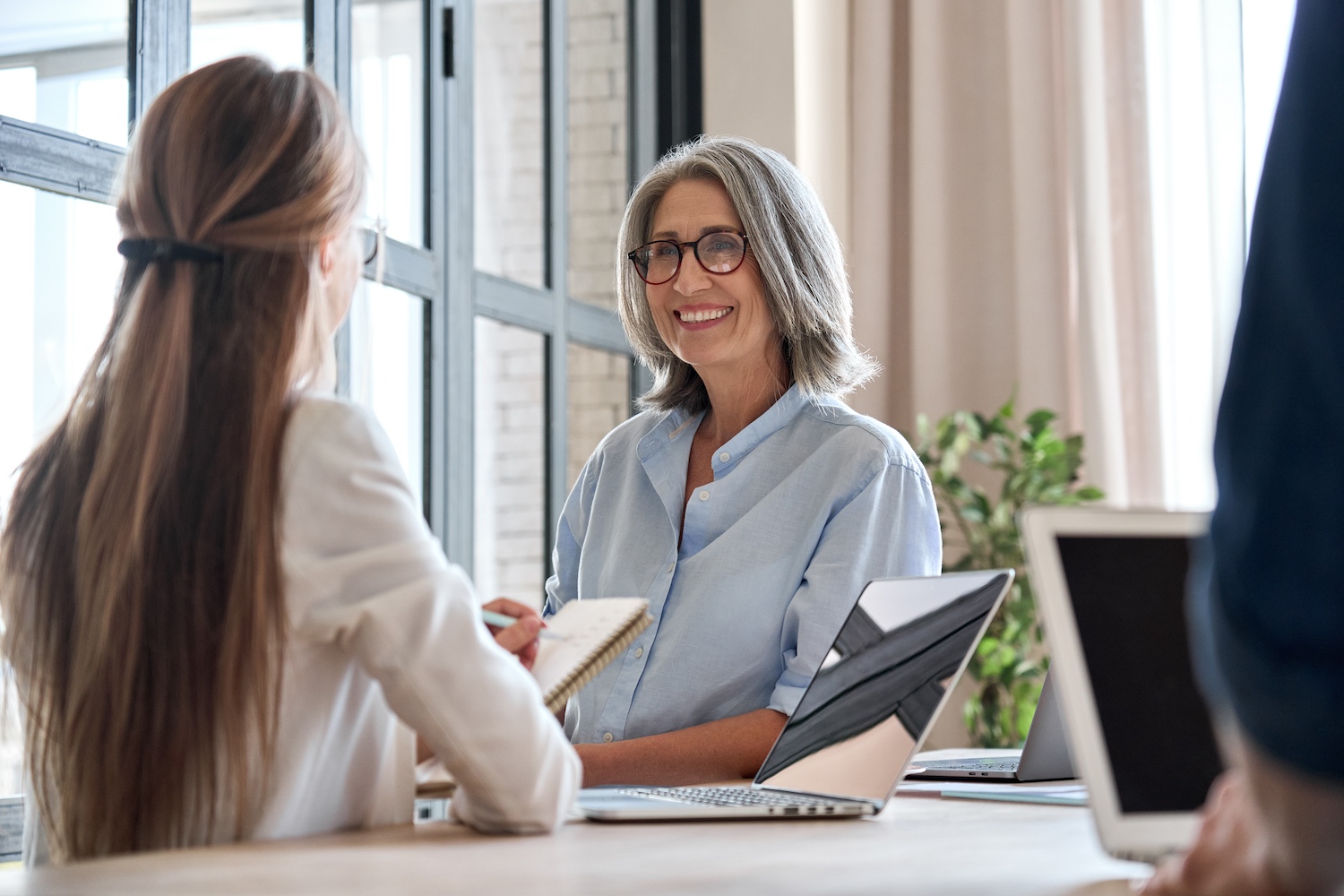 Senior business woman working on laptop with assistant writing notes.