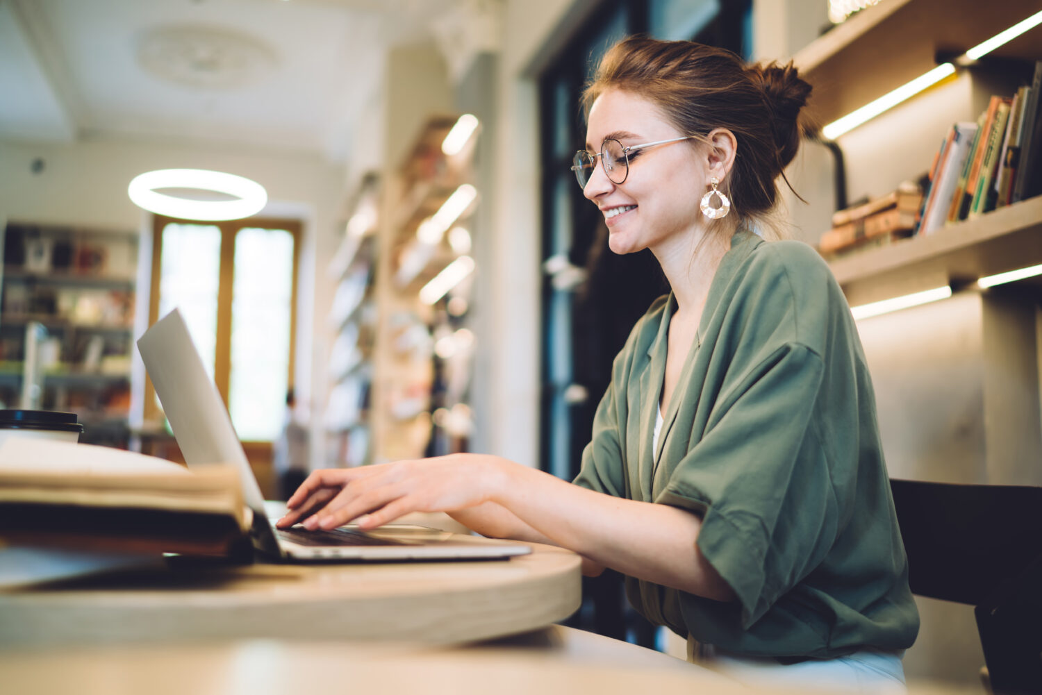 Cheerful young freelance woman typing on laptop in library