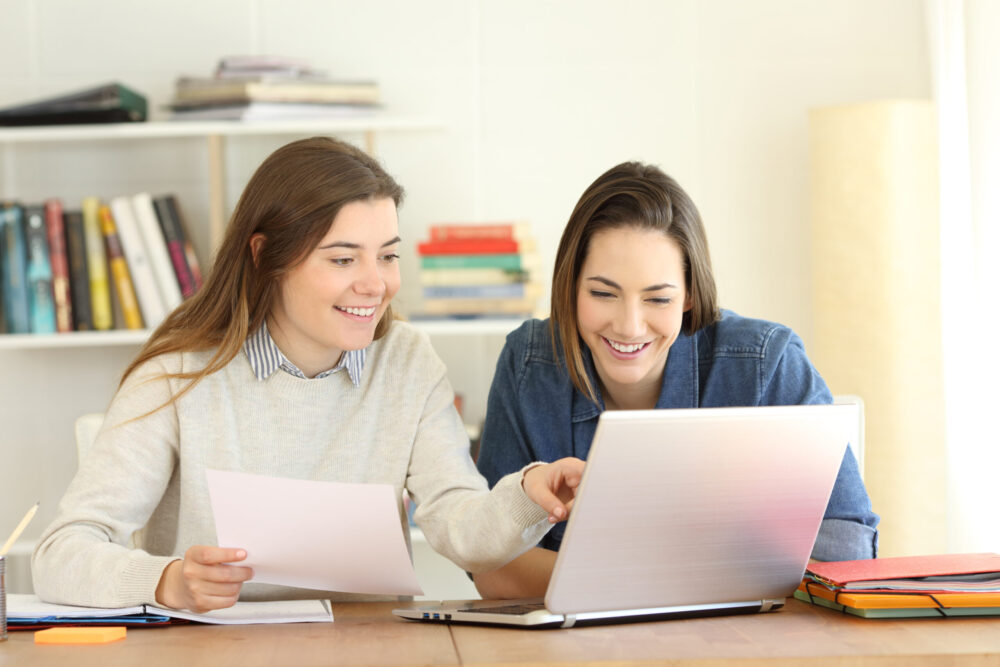 Two students learning together on line comparing notes with a laptop at home