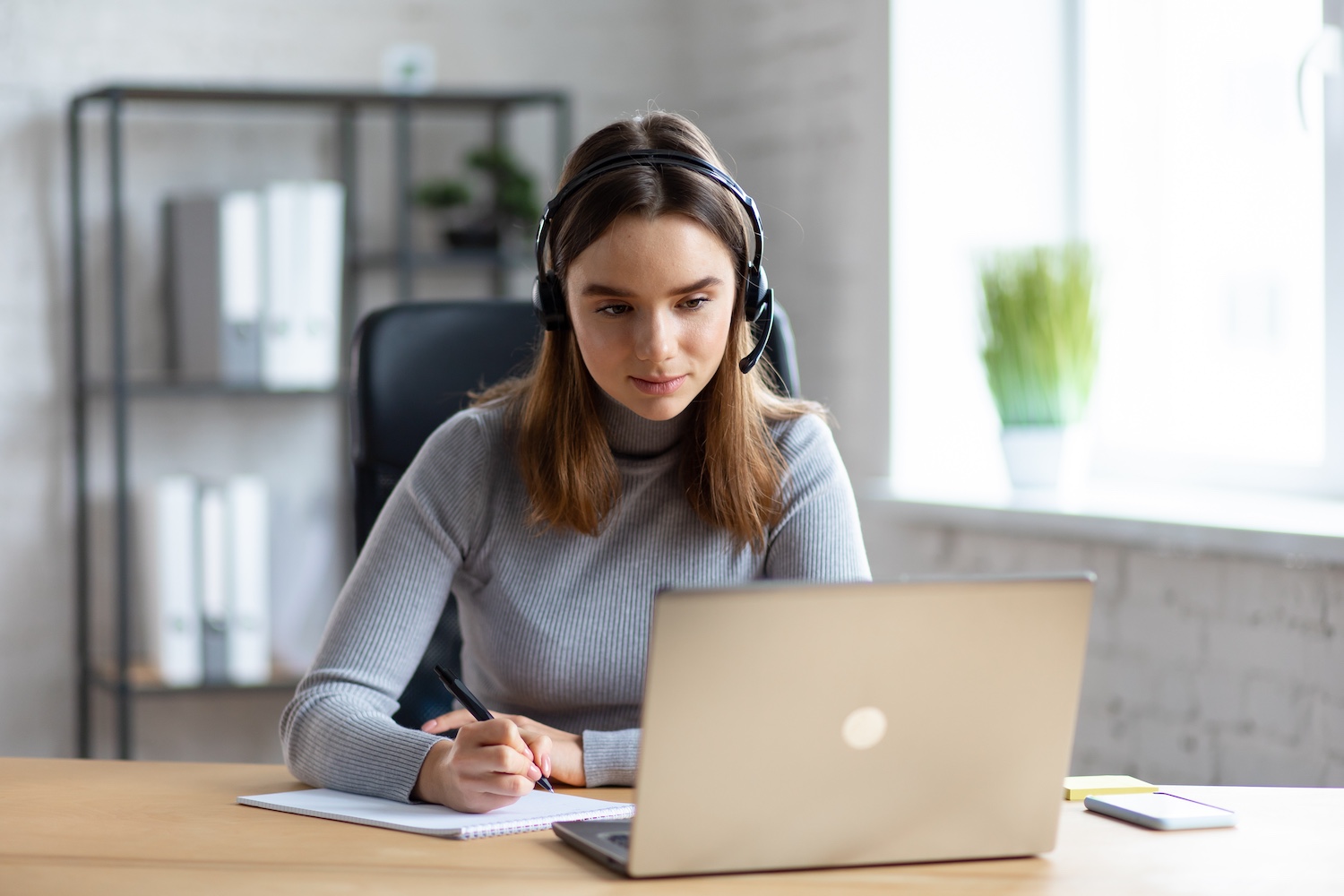 Beautiful young girl studying online using laptop web camera, writing lecture in notebook.Online education, remote working, home education.Online meeting,video call, video conference, courses online