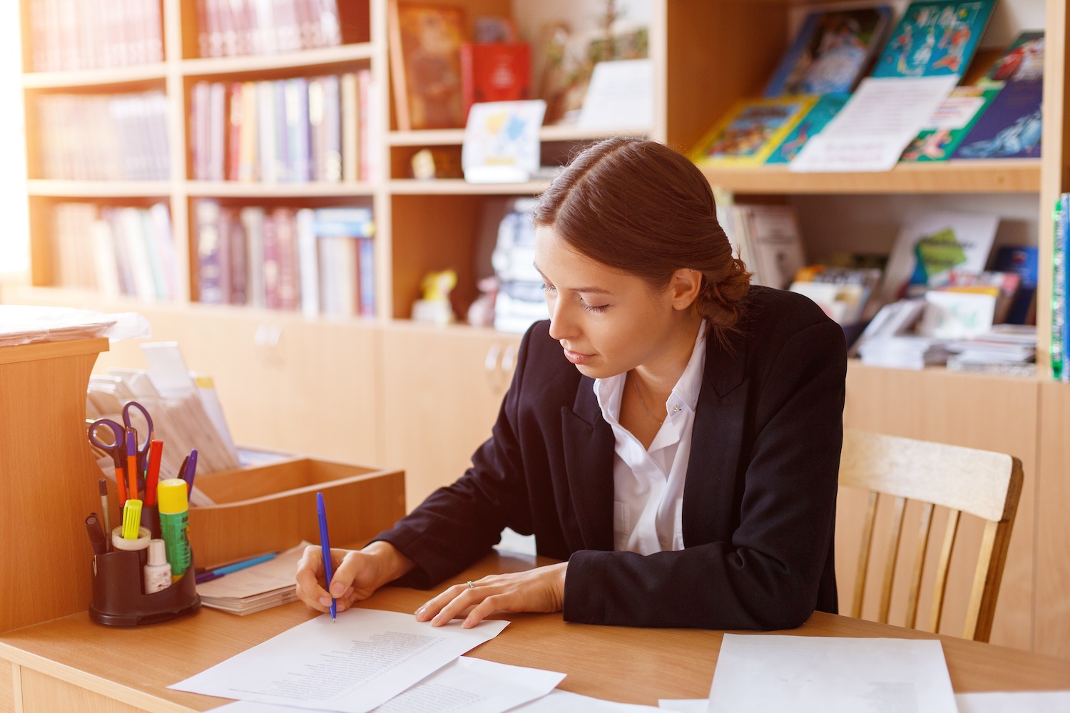 Office, young business woman signs documents in white shirt sitting at table. Caucasian girl works in the office and is engaged in the preparation of reports and the performance of official duties