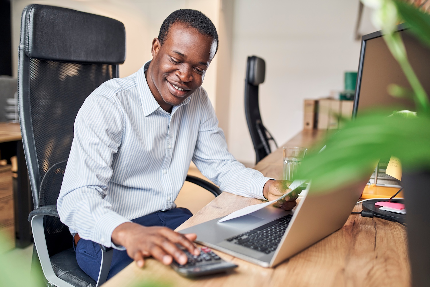 Smiling young businessman calculating business income doing paperwork in office