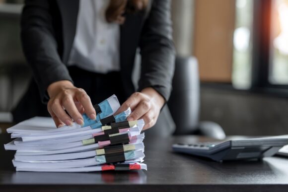 Businesswoman hands working in Stacks of paper files for searching and checking unfinished document achieves on folders papers